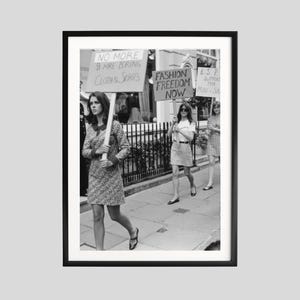 May include: Monochrome framed print showing women protesting with placards. One sign says "NO MORE BOREING CLOTHES SCOPES". Another reads "FASHION FREEDOM NOW". The women are dressed in dresses and skirts.
