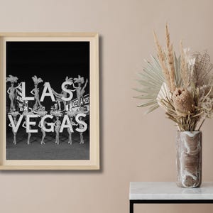 May include: Black and white framed print featuring the word "LAS VEGAS" in large, illuminated letters. The image includes showgirls and a vintage aesthetic, evoking a sense of classic entertainment and the iconic city.