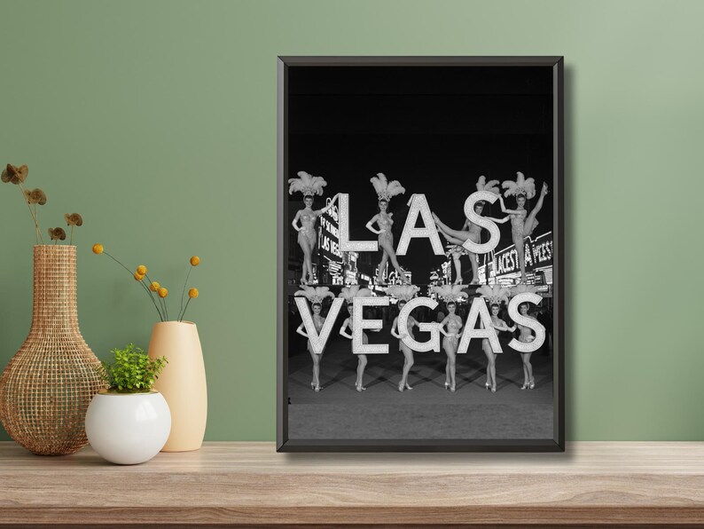 May include: Black and white framed print featuring the iconic "Las Vegas" sign with showgirls. The sign's letters are adorned with showgirls in elaborate costumes. The image evokes a vintage, retro aesthetic.
