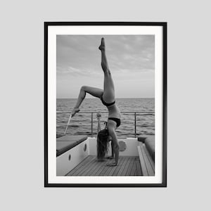 Peut inclure: Tirage encadr&eacute; en noir et blanc d'une personne faisant le poirier sur un bateau. La personne porte un bikini noir, avec la mer et le ciel en arri&egrave;re-plan. L'image est encadr&eacute;e dans un cadre noir.