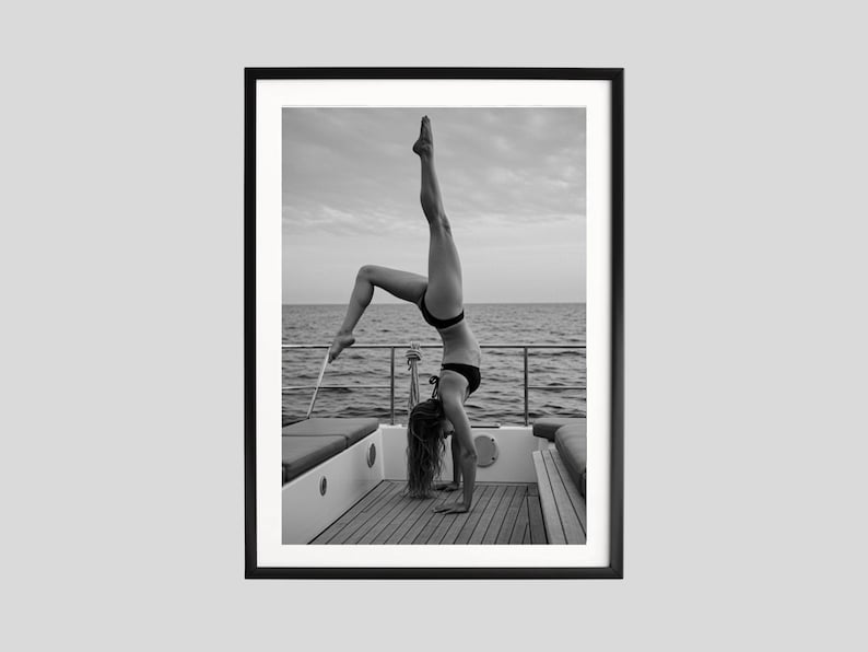 Peut inclure: Tirage encadr&eacute; en noir et blanc d'une personne faisant le poirier sur un bateau. La personne porte un bikini noir, avec la mer et le ciel en arri&egrave;re-plan. L'image est encadr&eacute;e dans un cadre noir.