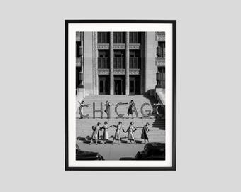 May include: Black and white framed photograph featuring the word "CHICAGO" in large letters on a building's steps. Several women in dresses and hats pose with the letters. The image is framed in a black border.