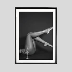 May include: Monochrome framed print showing a person's legs and torso, with a champagne glass. The person is reclining with legs raised. The image has a high-contrast, artistic aesthetic.