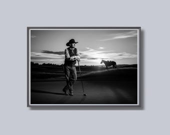 May include: Black and white framed photograph of a cowboy on a golf course. The cowboy, wearing a hat and vest, leans on a golf club. A horse stands in the background under a sunset sky. The image is a study in contrasts.