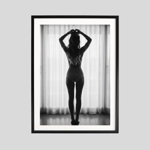 Pode incluir: Impressão de arte emoldurada em preto e branco. A imagem apresenta uma silhueta de uma pessoa em pé em frente a uma janela com cortinas transparentes. A pessoa é vista por trás, com os braços levantados acima da cabeça.