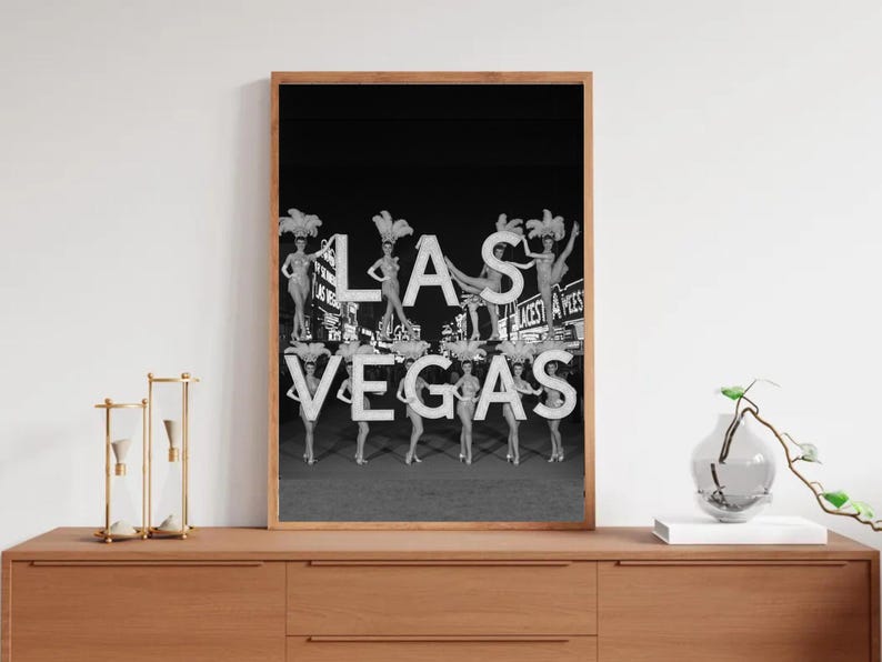 May include: Black and white framed print featuring the word "LAS VEGAS" with showgirls posing on the letters. The image has a vintage aesthetic, with the showgirls wearing elaborate headdresses and costumes. The background is a dark night sky.