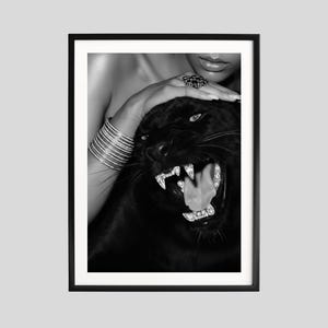 Op de afbeelding: Zwart-wit ingelijste print met een brullende panter met sprankelende versieringen. Een hand met zilveren armbanden en een ring rust op de kop van de panter. De afbeelding heeft een high-contrast, glamoureuze uitstraling.