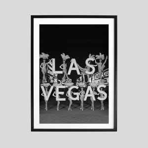 May include: Black and white framed print featuring the word "LAS VEGAS" with showgirls posing on and around the letters. The image captures a vintage aesthetic, evoking the glamour of Las Vegas.
