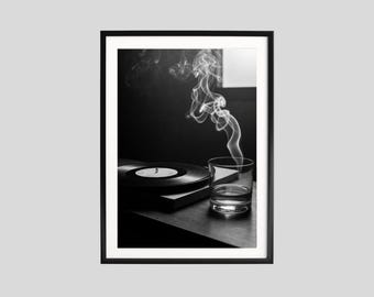 Könnte beinhalten: Schwarz-weiß gerahmtes Foto mit einer Schallplatte, einem Glas Wasser und Rauchschwaden. Das Bild hat eine nostalgische Ausstrahlung, mit Fokus auf Musik und Entspannung in einer dunklen Umgebung.
