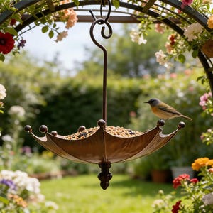 May include: A bronze-colored, umbrella-shaped bird feeder filled with seeds, suspended from a decorative metal arch. A small bird perches on the feeder's edge. The arch is adorned with colorful flowers, set against a blurred garden backdrop.