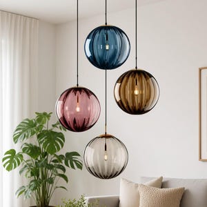 May include: A set of four spherical glass pendant lights suspended at varying heights. The globes feature vertical ribbed textures and come in translucent blue, amber, pink, and grey, each containing a single visible light bulb inside.