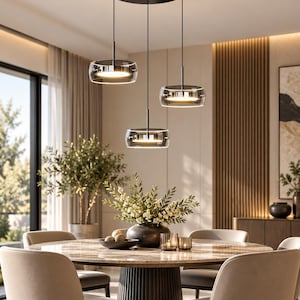 Puede incluir: Una lámpara colgante de tres luces con soportes circulares negros y pantallas de vidrio transparente con fuentes de luz internas, suspendida de un dosel negro sobre una mesa de comedor redonda con cuatro sillas tapizadas.