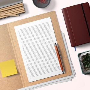 May include: A composition notebook with lined paper and a pen rests on a brown folder. A yellow sticky note is attached to the folder. A maroon journal and a small potted plant are also visible.
