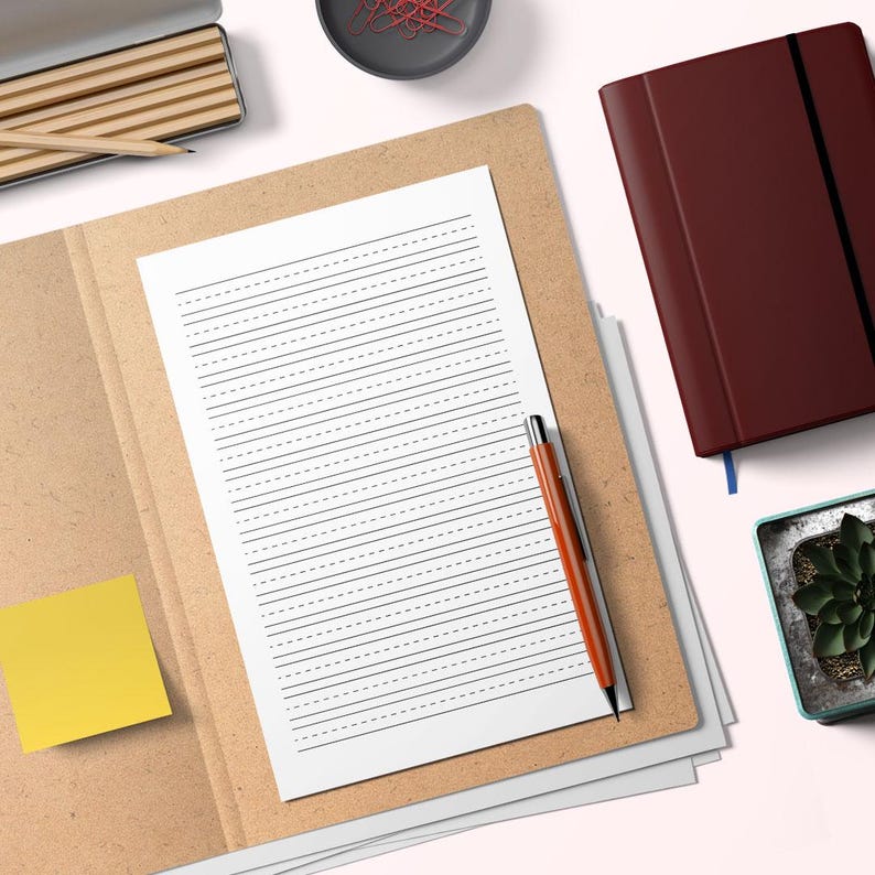 May include: A composition notebook with lined paper and a pen rests on a brown folder. A yellow sticky note is attached to the folder. A maroon journal and a small potted plant are also visible.
