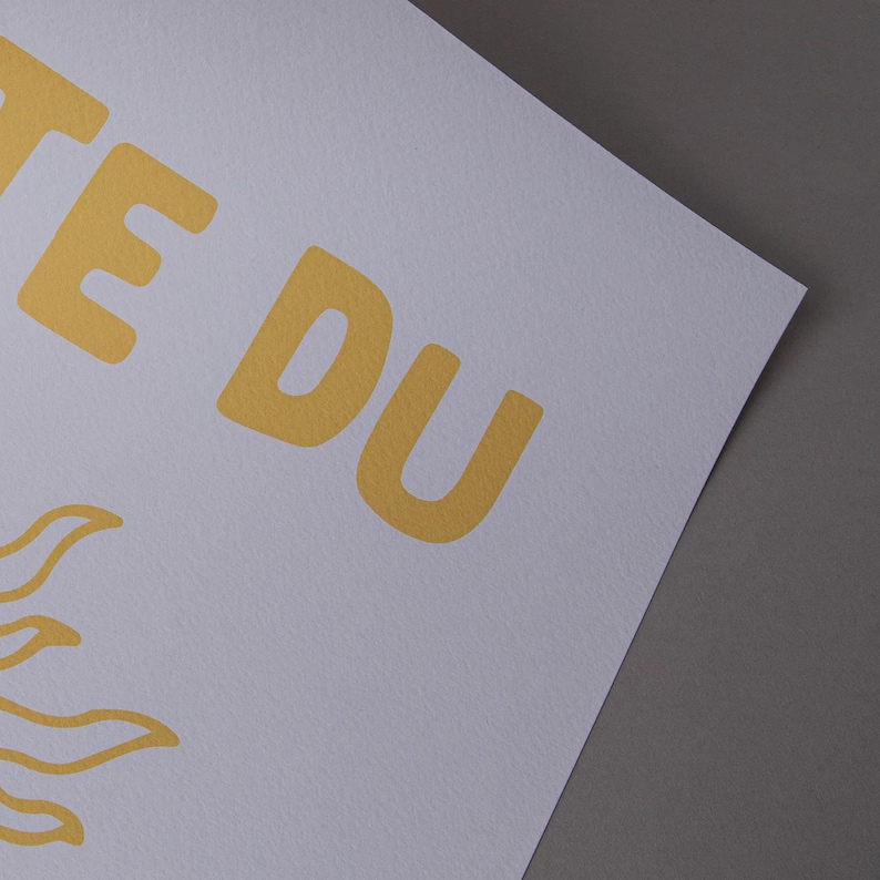 May include: A white print with yellow text and a sun graphic. The text reads "TE DU" in a bold, sans-serif font. The sun graphic is in the lower left corner. The print is on a white, textured paper.