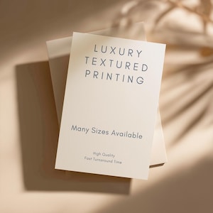 May include: Cream-coloured cards with the text "LUXURY TEXTURED PRINTING" in dark blue. Below, it reads "Many Sizes Available", "High Quality", and "Fast Turnaround Time". The cards are on a light beige surface.
