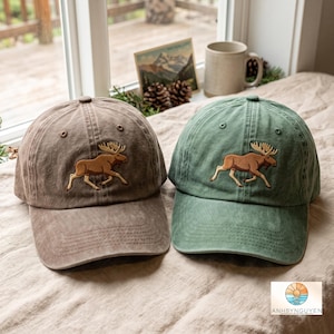 May include: Two baseball caps, one in a muted brown and one in a sage green, each featuring an embroidered brown moose graphic on the front panel. Both caps have a structured crown, a curved brim with stitched detailing, and eyelets for ventilation.