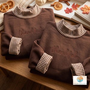 Puede incluir: Dos sudaderas de manga larga en color marrón oscuro con cuello alto y puños con estampado de cuadros vichy en marrón y blanco. La palabra thankful está bordada en letra cursiva en el pecho de cada prenda junto a un pequeño corazón.