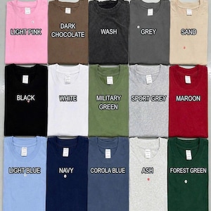 Puede incluir: Una tabla de colores de camisetas que muestra quince camisetas de cuello redondo dobladas en varios colores, incluyendo rosa claro, chocolate oscuro, lavado, gris, arena, negro, blanco, verde militar, gris deportivo, granate, azul claro, marino, azul corola, ceniza y verde bosque.