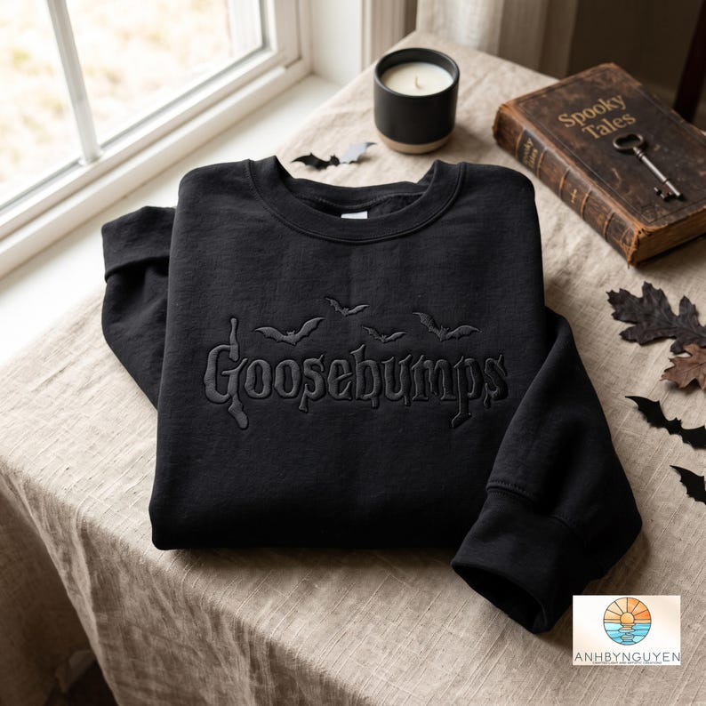 May include: A black crewneck sweatshirt featuring the word Goosebumps embroidered in a matching black thread across the chest, accompanied by small embroidered bat silhouettes flying above the text.