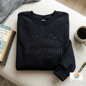 以下が含まれることがあります： ゴシック体のフォントで「Neurology Department」と刺繍され、その周囲に小さなコウモリのシルエットが刺繍された黒いクルーネックのスウェットシャツ。刺繍はスウェットシャツの黒い生地と同系色で施されています。