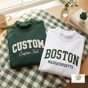 Puede incluir: Una sudadera verde oscuro con la palabra CUSTOM en letras beige y Custom Text en cursiva, junto a una sudadera blanca con la palabra BOSTON en letras verde oscuro y MASSACHUSETTS en letras negras más pequeñas.
