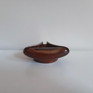 May include: A brown ceramic ashtray with a smooth, glossy finish and a distinct three-pointed, curved rim design. The object features a deep, rounded basin and a solid base, showcasing a gradient of dark and light brown tones across its surface.