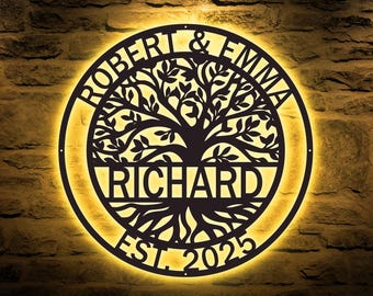 May include: A circular, illuminated metal sign with a tree of life design. The sign features the names "ROBERT & EMMA" at the top, "RICHARD" in the center, and "EST. 2025" at the bottom. The sign is mounted on a textured, brown brick wall.