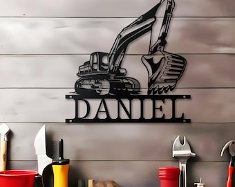 May include: Black metal excavator wall art with the name "DANIEL" cut out below. The excavator features a bucket, arm, and treads. The background is a light grey wooden wall with tools.