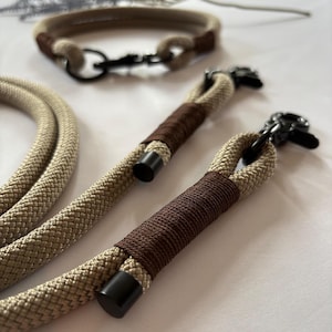 May include: Tan and brown dog collar and leash set. The collar and leash are made of a thick, woven rope material. The leash has a brown wrapped handle and black metal hardware. The collar has a matching brown accent.