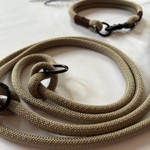 May include: Tan rope dog leash and matching collar set. The leash is coiled and features a black metal ring and clasp. The collar has a brown accent and a black metal clasp. The set is designed for pet owners.