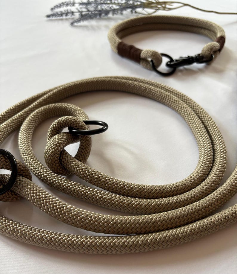 May include: Tan rope dog leash and matching collar set. The leash is coiled and features a black metal ring and clasp. The collar has a brown accent and a black metal clasp. The set is designed for pet owners.