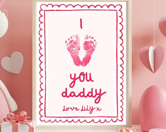 Può includere: Una stampa incorniciata con sfondo rosa presenta due impronte di piedi rosa sopra le parole "I you daddy" in un carattere scritto a mano. Il testo "Love Lily x" è in basso. La cornice ha un bordo smerlato.