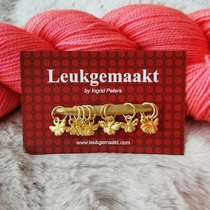 May include: A set of 7 gold bee stitch markers on a red card with white polka dots. The card says "Leukegemaakt by Ingrid Peters" and "www.leukegemaakt.com".