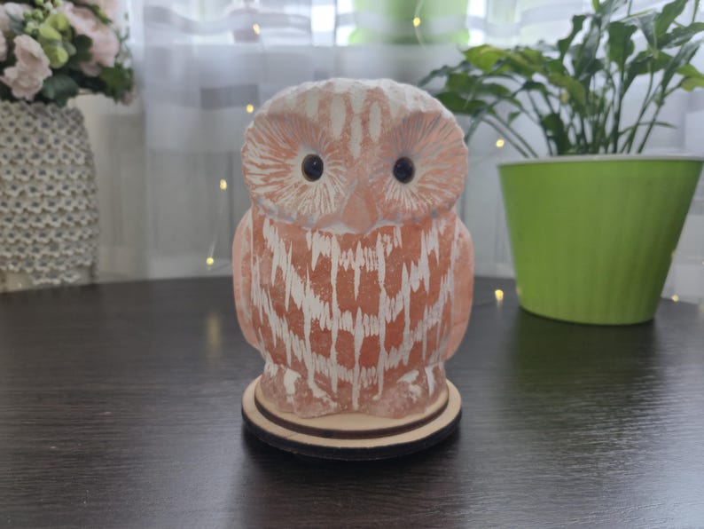 May include: A decorative owl figurine in shades of orange and white, standing on a wooden base. The owl has large, dark eyes and a textured surface. The figurine is a decorative item.