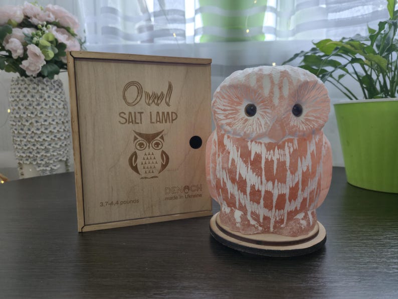 May include: An owl-shaped salt lamp with a wooden base and a wooden box. The lamp is peach-colored with white streaks, and the box is engraved with an owl design and the words "Owl Salt Lamp". The lamp weighs 3.7-4.4 pounds.