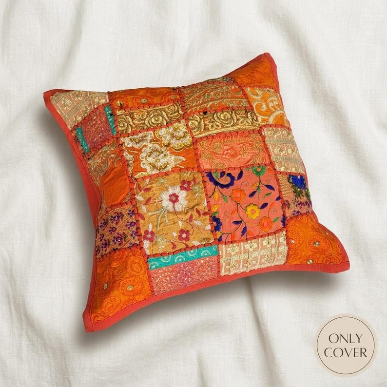 May include: A square throw pillow cover featuring a patchwork design of various orange, gold, and red fabric squares. The fabric squares are decorated with intricate floral embroidery, metallic gold thread accents, and small sequins.