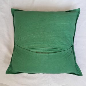 May include: A square throw pillow in a solid forest green color. The pillow features a horizontal overlapping fabric flap across the center, creating a pocket-like design. The fabric has a visible texture with subtle horizontal lines throughout.