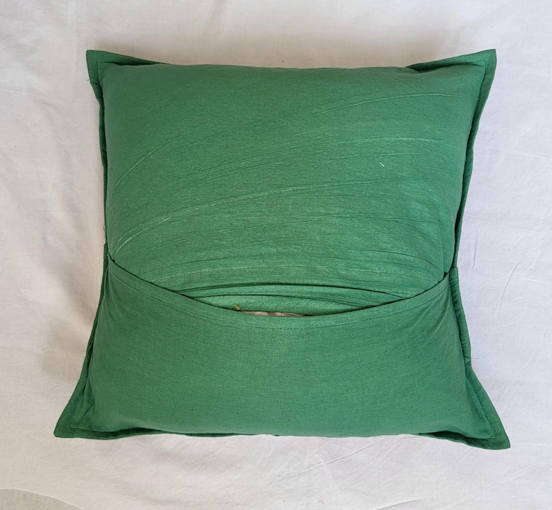 May include: A square throw pillow in a solid forest green color. The pillow features a horizontal overlapping fabric flap across the center, creating a pocket-like design. The fabric has a visible texture with subtle horizontal lines throughout.