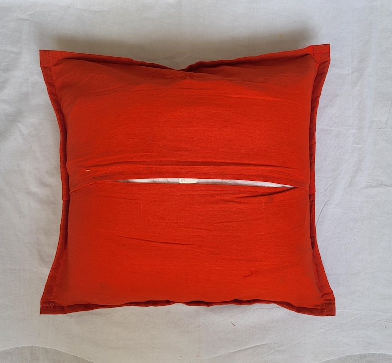 May include: A square throw pillow cover in a solid, vibrant orange color. The cover features a central horizontal opening with an overlapping fabric flap design, revealing a glimpse of the white inner pillow insert through the middle gap.