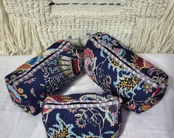 Pode incluir: Três bolsas acolchoadas em tecido azul-escuro com um padrão floral e paisley colorido. Cada bolsa possui um fecho de correr com acabamento às riscas, uma forma cilíndrica e uma textura suave e pespontada em toda a superfície exterior.