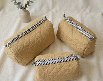May include: Three mustard yellow quilted pouches with a diamond-stitched pattern and a black and white striped zipper closure. Each rectangular bag features a soft fabric construction and a secure top zipper, providing a consistent design.