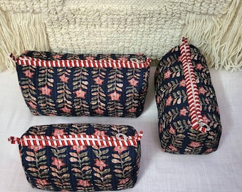 May include: Three navy blue cosmetic bags with a floral pattern in pink and green. Each bag has a red and white striped zipper and trim. The bags are different sizes and shapes, with one standing upright.