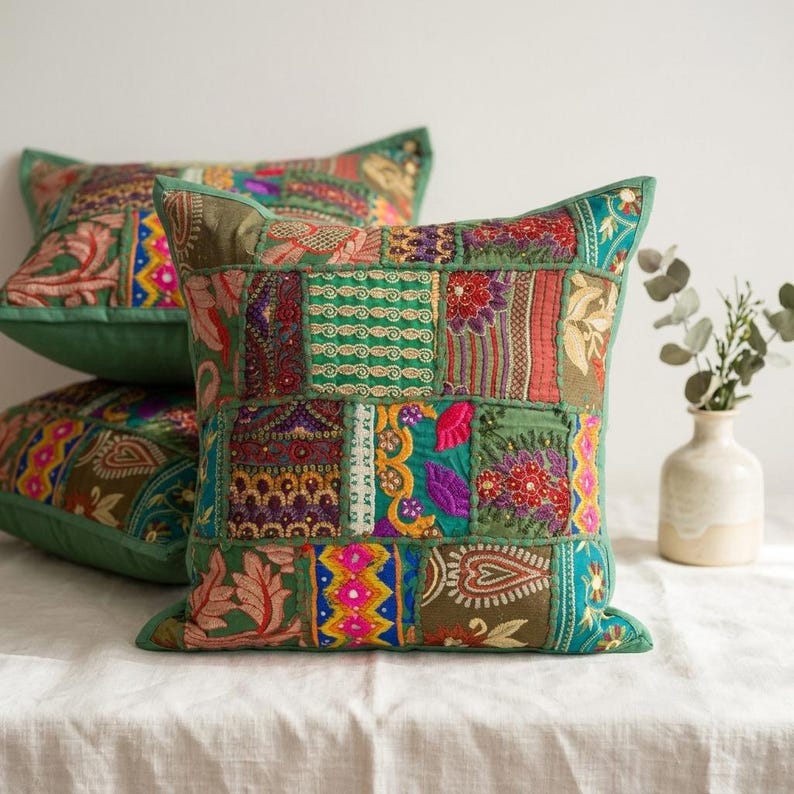 May include: Two square throw pillows featuring a patchwork design of various embroidered fabrics in shades of green, red, yellow, and pink. The pillows display intricate floral and geometric patterns with visible stitching and decorative embellishments.