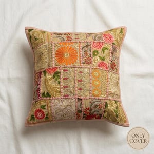 May include: A square decorative pillow cover featuring a patchwork design of beige fabric panels with intricate embroidery, gold metallic thread accents, and floral motifs in orange, pink, and green. The panels are joined by pink piping.