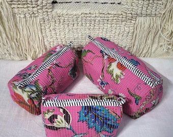 Pode incluir: Três nécessaires rosa com um padrão floral em azul, verde e vermelho. As bolsas têm uma borda listrada em preto e branco e um fecho de zíper. As bolsas são de tamanhos diferentes e estão dispostas juntas.