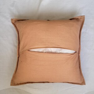 May include: A square throw pillow cover in a solid light brown color. The cover features a central horizontal envelope-style opening that reveals a white inner pillow insert. The fabric has a visible woven texture with stitched edges.