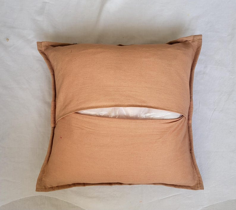 May include: A square throw pillow cover in a solid light brown color. The cover features a central horizontal envelope-style opening that reveals a white inner pillow insert. The fabric has a visible woven texture with stitched edges.