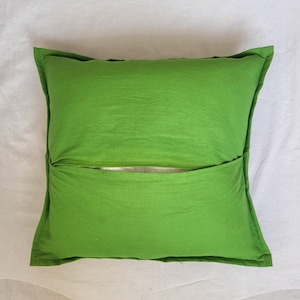 May include: A square, bright green throw pillow cover featuring an envelope-style closure on the back. The fabric has a smooth, matte texture with visible stitched seams along the edges, showcasing a simple, functional design for a cushion.