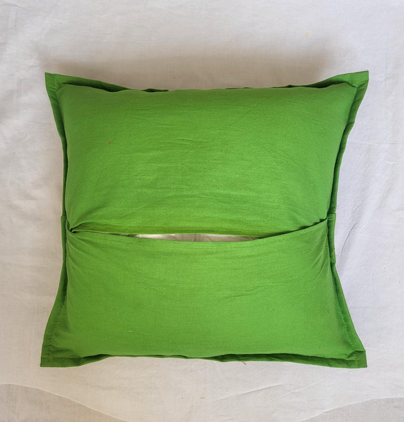 May include: A square, bright green throw pillow cover featuring an envelope-style closure on the back. The fabric has a smooth, matte texture with visible stitched seams along the edges, showcasing a simple, functional design for a cushion.